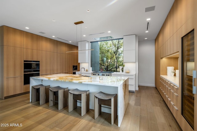 kitchen with pendant lighting, a large island, double oven, light stone counters, and light hardwood / wood-style floors