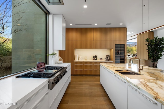 kitchen with sink, white cabinets, stainless steel gas cooktop, light stone counters, and light wood-type flooring