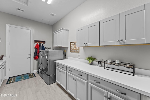 clothes washing area with cabinets, washer and clothes dryer, and light hardwood / wood-style flooring