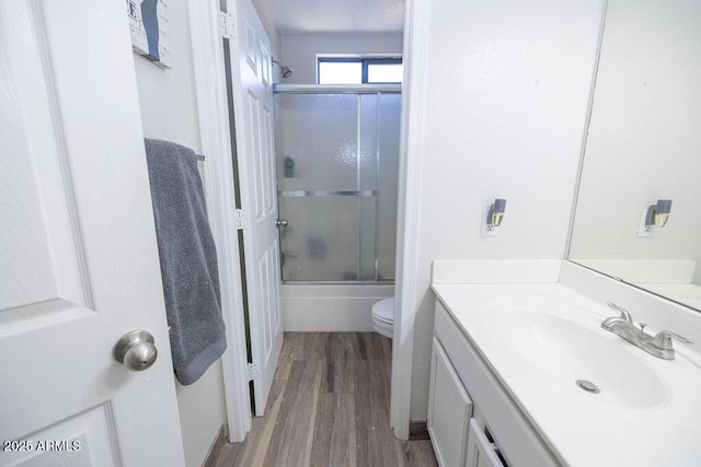 full bathroom with vanity, hardwood / wood-style floors, shower / bath combination with glass door, and toilet