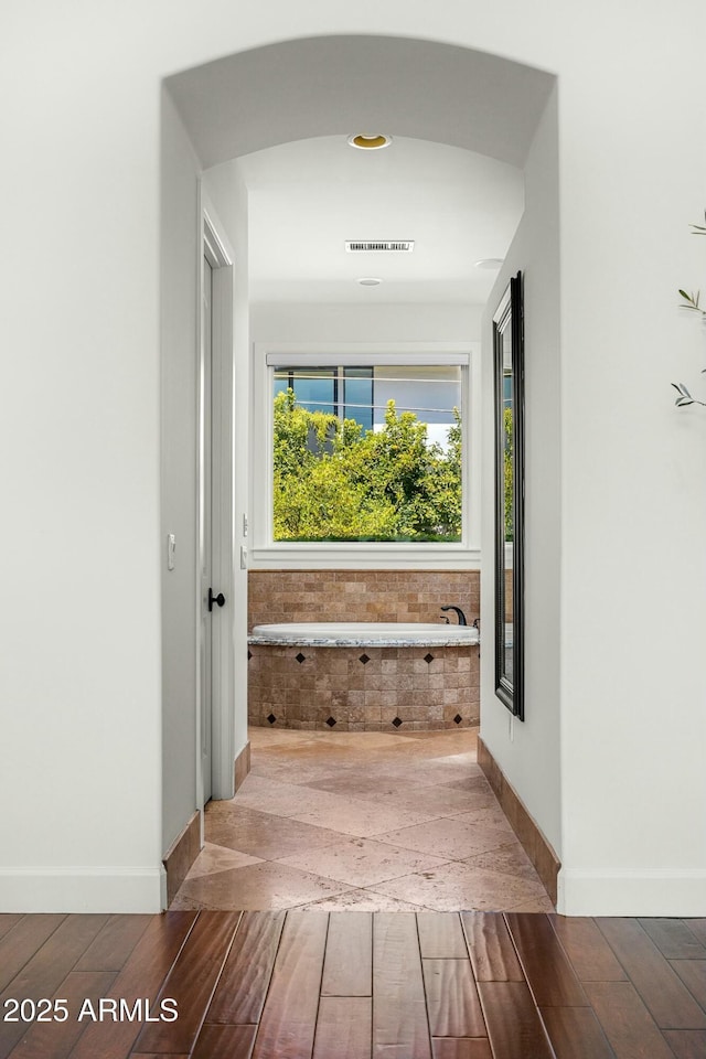 hall featuring arched walkways, visible vents, baseboards, and wood finished floors