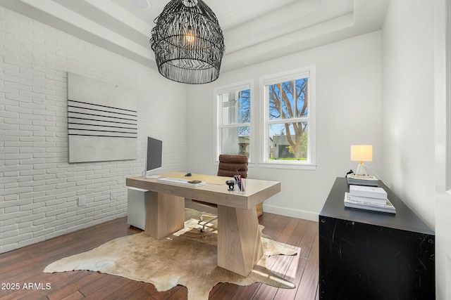 office with brick wall, wood-type flooring, a raised ceiling, and a notable chandelier