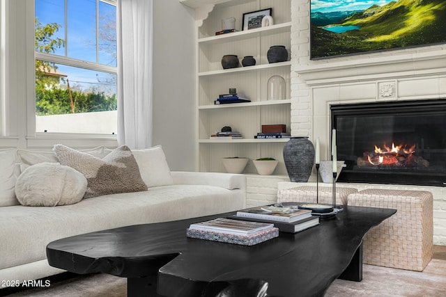 living area with built in shelves, a glass covered fireplace, and wood finished floors