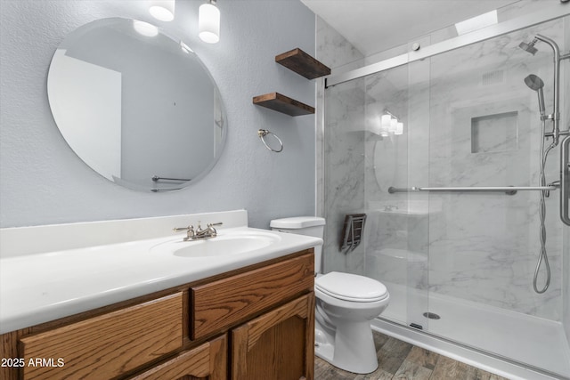 bathroom featuring wood-type flooring, toilet, a shower with shower door, and vanity