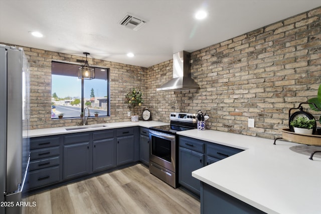 kitchen featuring blue cabinetry, wall chimney exhaust hood, sink, hanging light fixtures, and appliances with stainless steel finishes