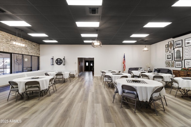 dining room featuring a drop ceiling, wood-type flooring, and brick wall