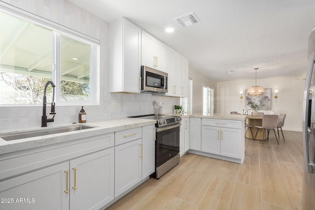 kitchen featuring sink, white cabinetry, appliances with stainless steel finishes, kitchen peninsula, and pendant lighting