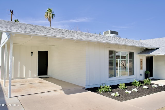 view of exterior entry featuring a patio area, cooling unit, and roof with shingles