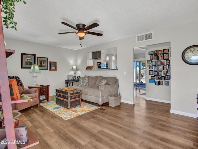 living room featuring hardwood / wood-style flooring, ceiling fan, and a textured ceiling