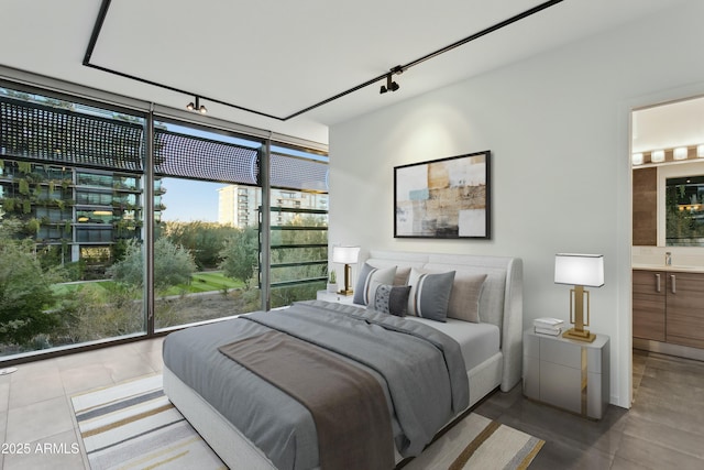 bedroom featuring tile patterned flooring, ensuite bath, a wall of windows, and rail lighting