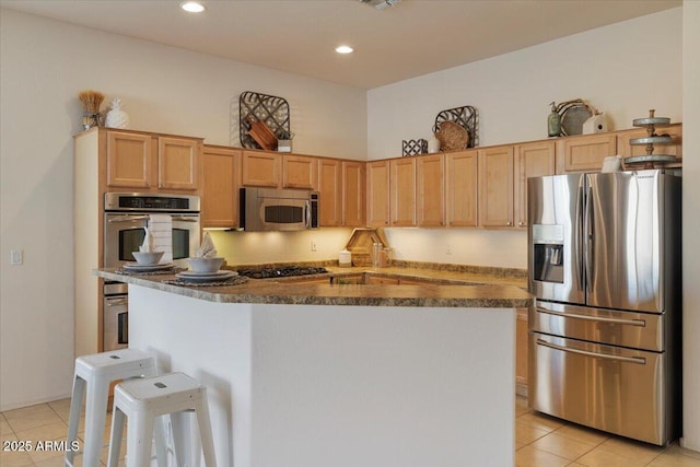 kitchen with light tile patterned floors, appliances with stainless steel finishes, light brown cabinetry, and a breakfast bar area