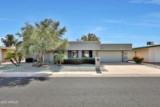 view of front of home featuring concrete driveway, central AC, an attached garage, and stucco siding