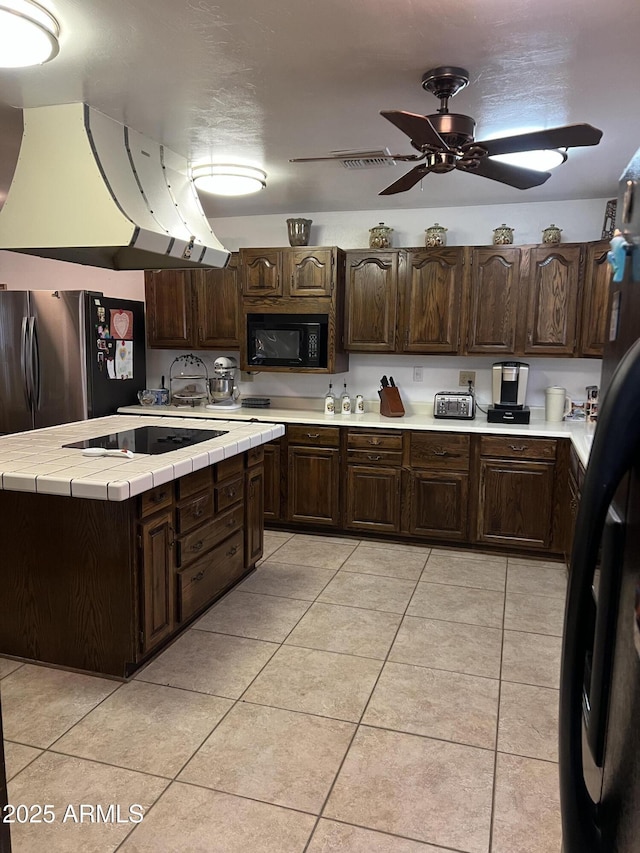 kitchen with light tile patterned floors, tile counters, black appliances, and dark brown cabinets