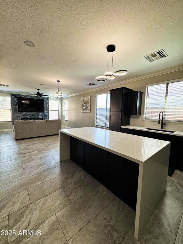 kitchen featuring a kitchen island, sink, hanging light fixtures, and crown molding