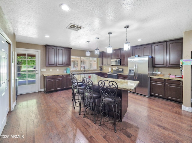 kitchen featuring stainless steel appliances, dark wood finished floors, dark brown cabinets, a kitchen breakfast bar, and a textured ceiling