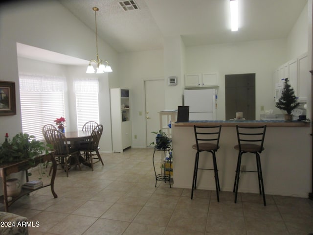 kitchen featuring hanging light fixtures, light tile patterned floors, a kitchen breakfast bar, white refrigerator, and white cabinets