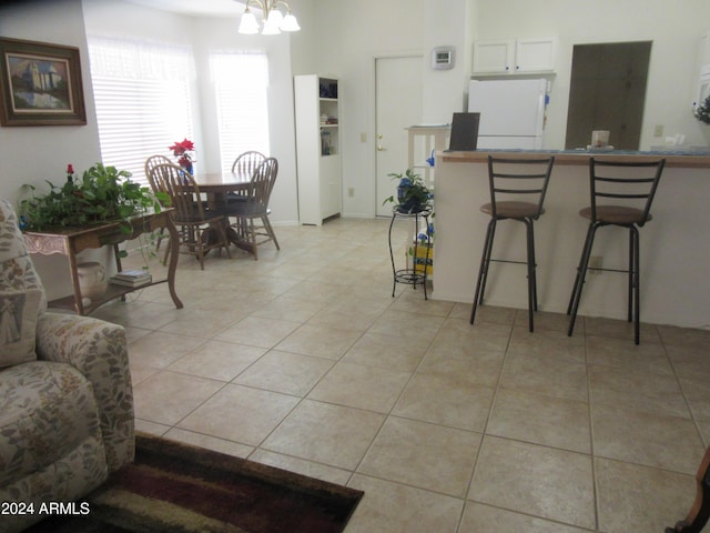 interior space with light tile patterned flooring, white cabinets, white fridge, a kitchen bar, and a chandelier