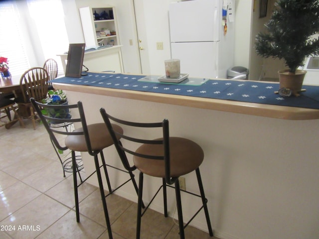 kitchen with a breakfast bar, white fridge, and tile patterned flooring