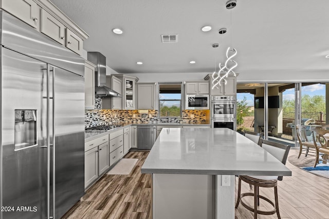 kitchen with wall chimney exhaust hood, decorative light fixtures, gray cabinets, and built in appliances