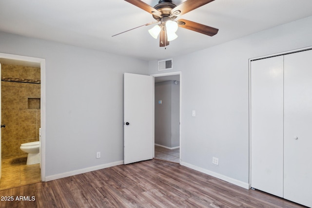 unfurnished bedroom with wood finished floors, visible vents, baseboards, ensuite bath, and a closet