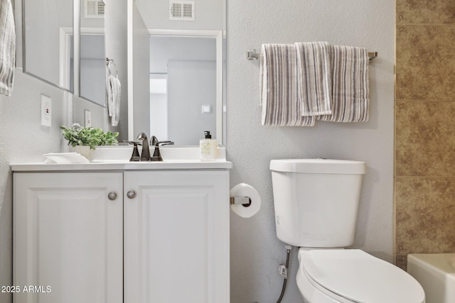 bathroom featuring visible vents, toilet, vanity, and a textured wall