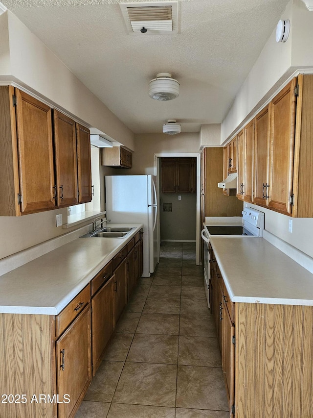 kitchen featuring a textured ceiling, dark tile patterned floors, white appliances, and sink