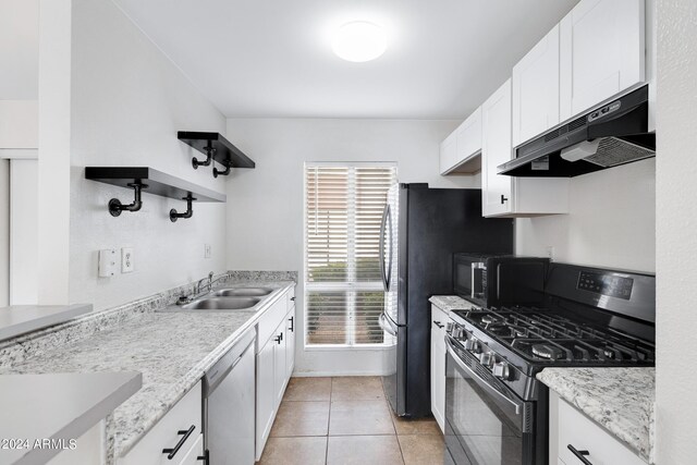 kitchen featuring appliances with stainless steel finishes, light stone counters, sink, light tile patterned floors, and white cabinetry