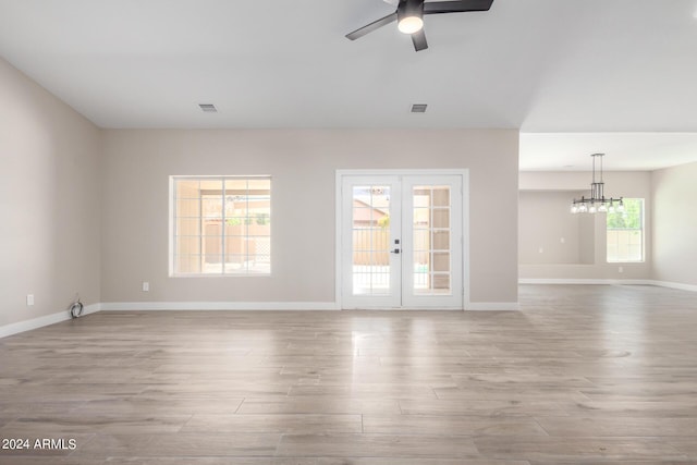 unfurnished living room with ceiling fan with notable chandelier, french doors, and light wood-type flooring