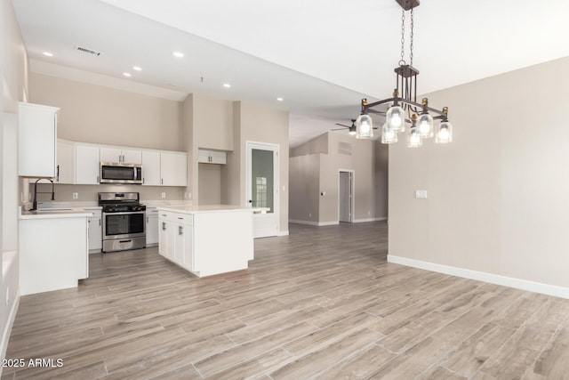 kitchen featuring appliances with stainless steel finishes, pendant lighting, white cabinetry, sink, and a center island