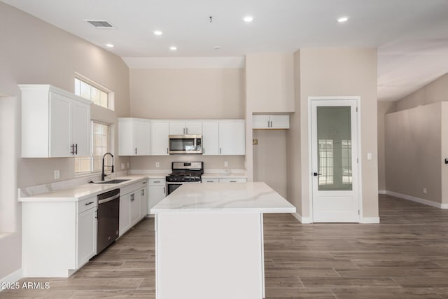 kitchen featuring sink, appliances with stainless steel finishes, white cabinetry, a center island, and light stone countertops