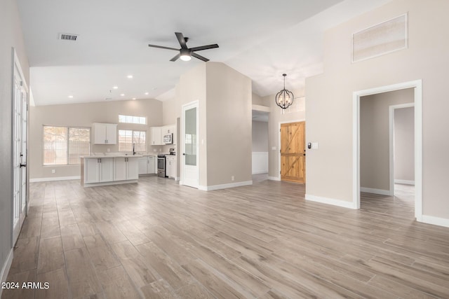 unfurnished living room with ceiling fan with notable chandelier, light hardwood / wood-style flooring, and high vaulted ceiling