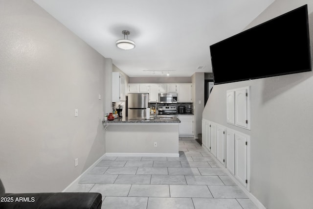 kitchen featuring appliances with stainless steel finishes, white cabinetry, backsplash, dark stone countertops, and kitchen peninsula