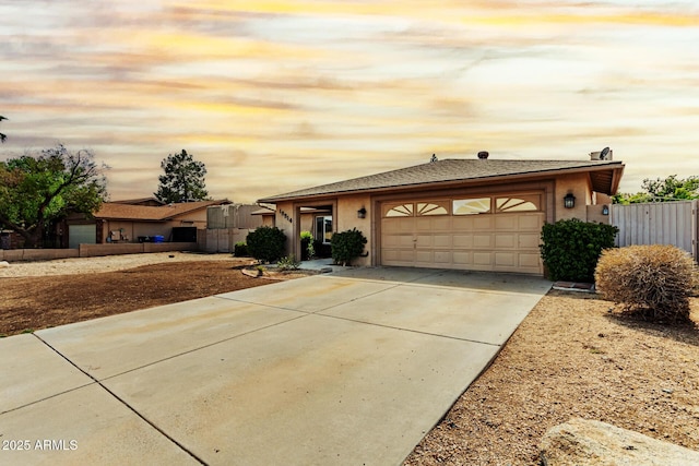 single story home with an attached garage, concrete driveway, fence, a shingled roof, and stucco siding