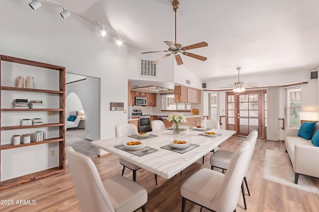 dining room featuring ceiling fan, track lighting, arched walkways, light wood-style flooring, and high vaulted ceiling