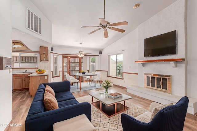 living area featuring a ceiling fan, light wood-style flooring, lofted ceiling, and a glass covered fireplace