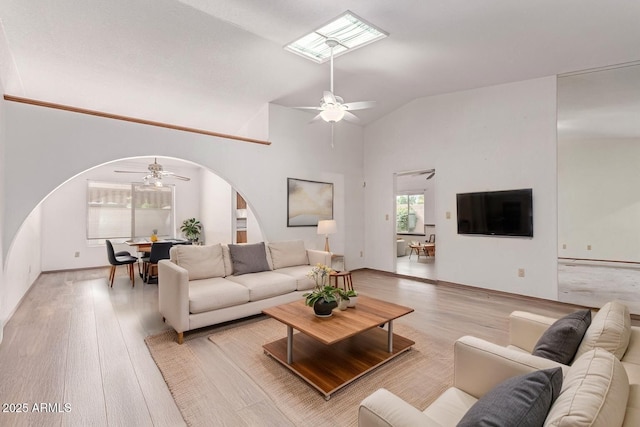 living area with arched walkways, a ceiling fan, light wood-style floors, and vaulted ceiling