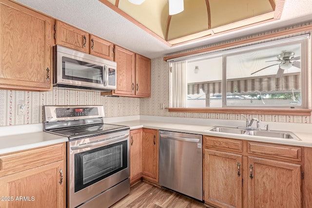 kitchen with stainless steel appliances, a sink, wallpapered walls, light countertops, and light wood finished floors