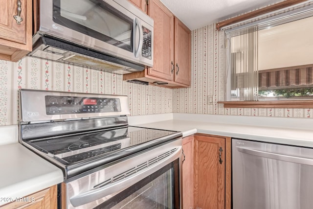 kitchen with stainless steel appliances, wallpapered walls, light countertops, and brown cabinets