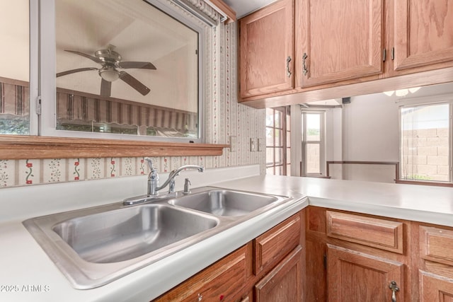 kitchen featuring a sink, light countertops, ceiling fan, wallpapered walls, and brown cabinetry