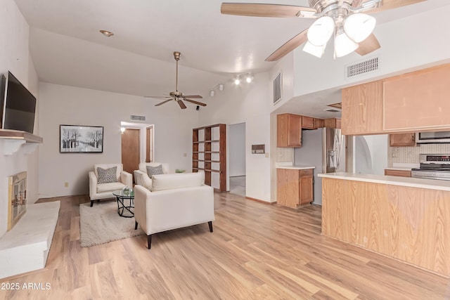 living area with ceiling fan, high vaulted ceiling, light wood-style floors, and a glass covered fireplace