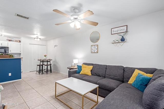 living area featuring light tile patterned flooring, visible vents, baseboards, and a ceiling fan