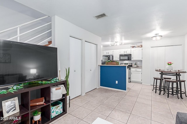 kitchen featuring visible vents, black microwave, stainless steel electric stove, light tile patterned floors, and white cabinetry