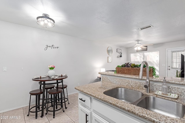 kitchen featuring visible vents, light stone countertops, light tile patterned floors, white cabinets, and a sink