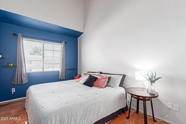 bedroom featuring a high ceiling, wood finished floors, and baseboards