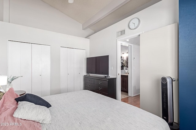 bedroom featuring visible vents, two closets, lofted ceiling, and wood finished floors