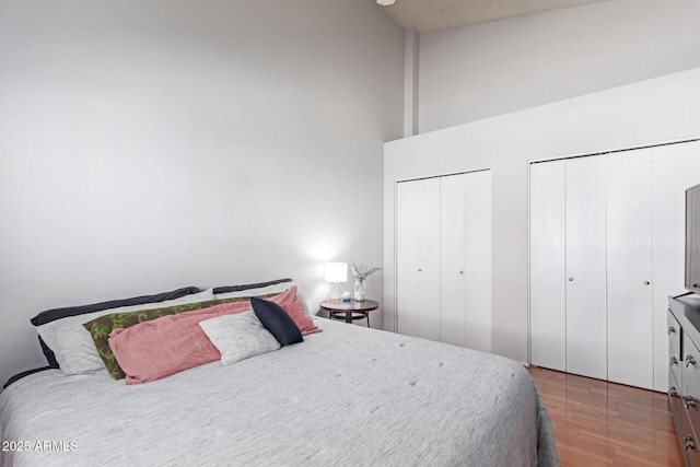 bedroom with two closets, wood finished floors, and a towering ceiling