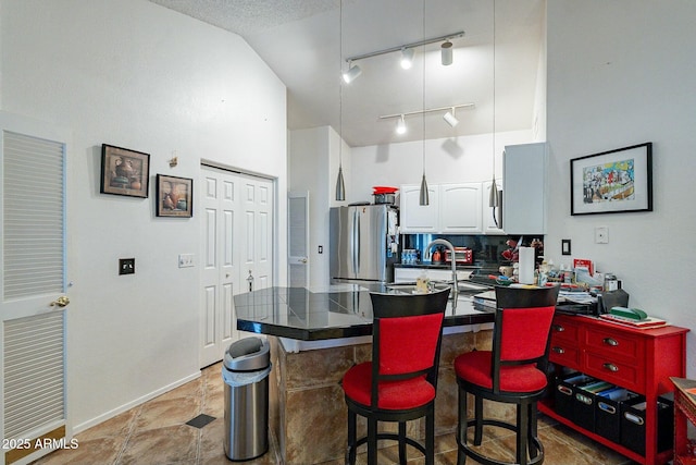 kitchen featuring a breakfast bar area, a peninsula, freestanding refrigerator, white cabinets, and a towering ceiling