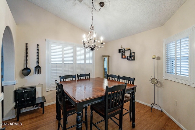 dining room featuring wood finished floors, baseboards, an inviting chandelier, vaulted ceiling, and a textured ceiling