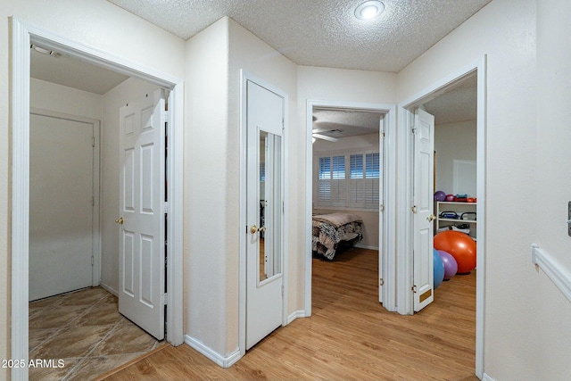 hallway with baseboards, light wood-style floors, and a textured ceiling