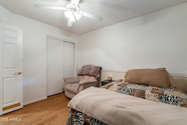 bedroom with a ceiling fan, baseboards, light wood-style flooring, a closet, and a textured ceiling